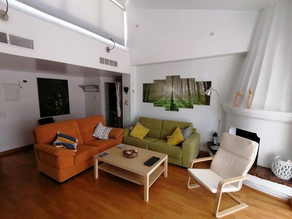 Ein geräumiges Wohnzimmer mit großem Fenster, einem grünen Sofa, einem orangen Sofa, einem weißen Sessel und einem Couchtisch.