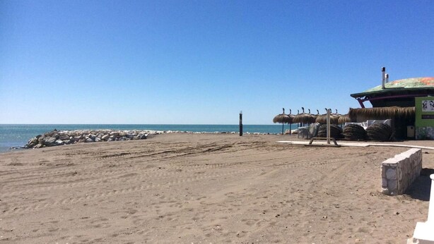 Ein Strand mit einer strohgedeckten Struktur, einem Sandbereich und einem klaren, blauen Himmel.