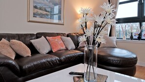A living room with a dark leather sofa, a white coffee table, and a vase with white flowers. - Riverview-2br-sleeps4-citycentre-parking-fastwifi (Aberdeen)