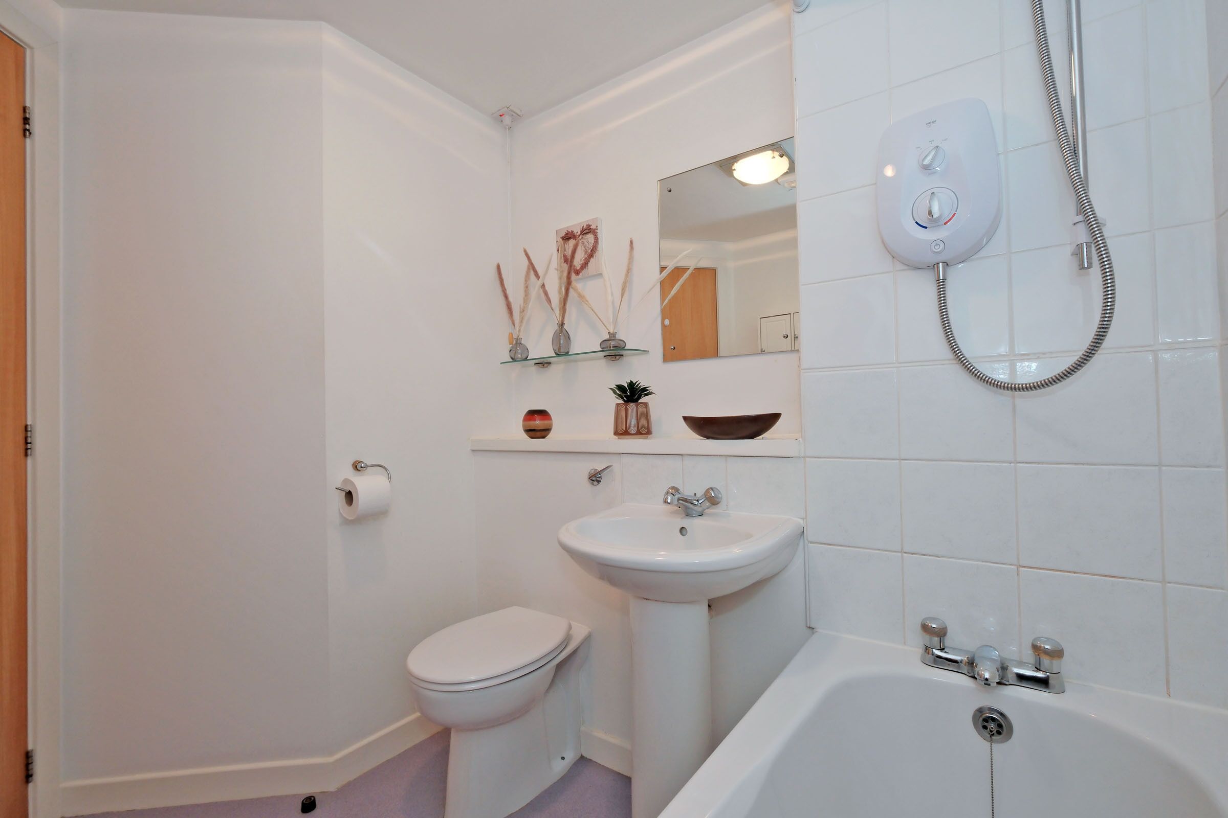 Ein Badezimmer mit Toilette, Waschbecken und Badewanne. Über dem Waschbecken befindet sich ein Spiegel und über der Badewanne ein Duschkopf.