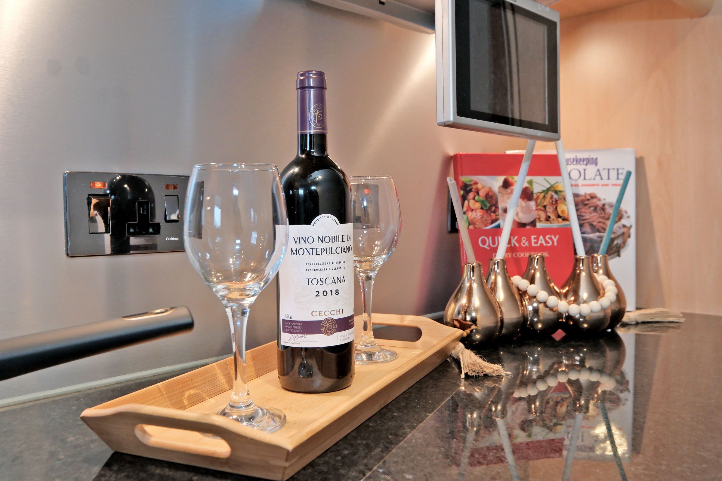 A bottle of wine on a tray with two glasses, a kitchen appliance, and a cookbook on the counter.