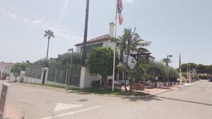 A building with a white facade, a flagpole, and a palm tree. - Beachfront Estepona Apartment with Pool, Terrace & Free Parking (Estepona)