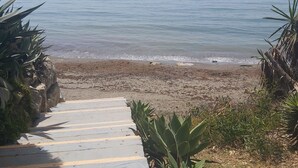 A beach with a wooden pathway leading to the shore, surrounded by tropical plants. - Beachfront Estepona Apartment with Pool, Terrace & Free Parking (Estepona)