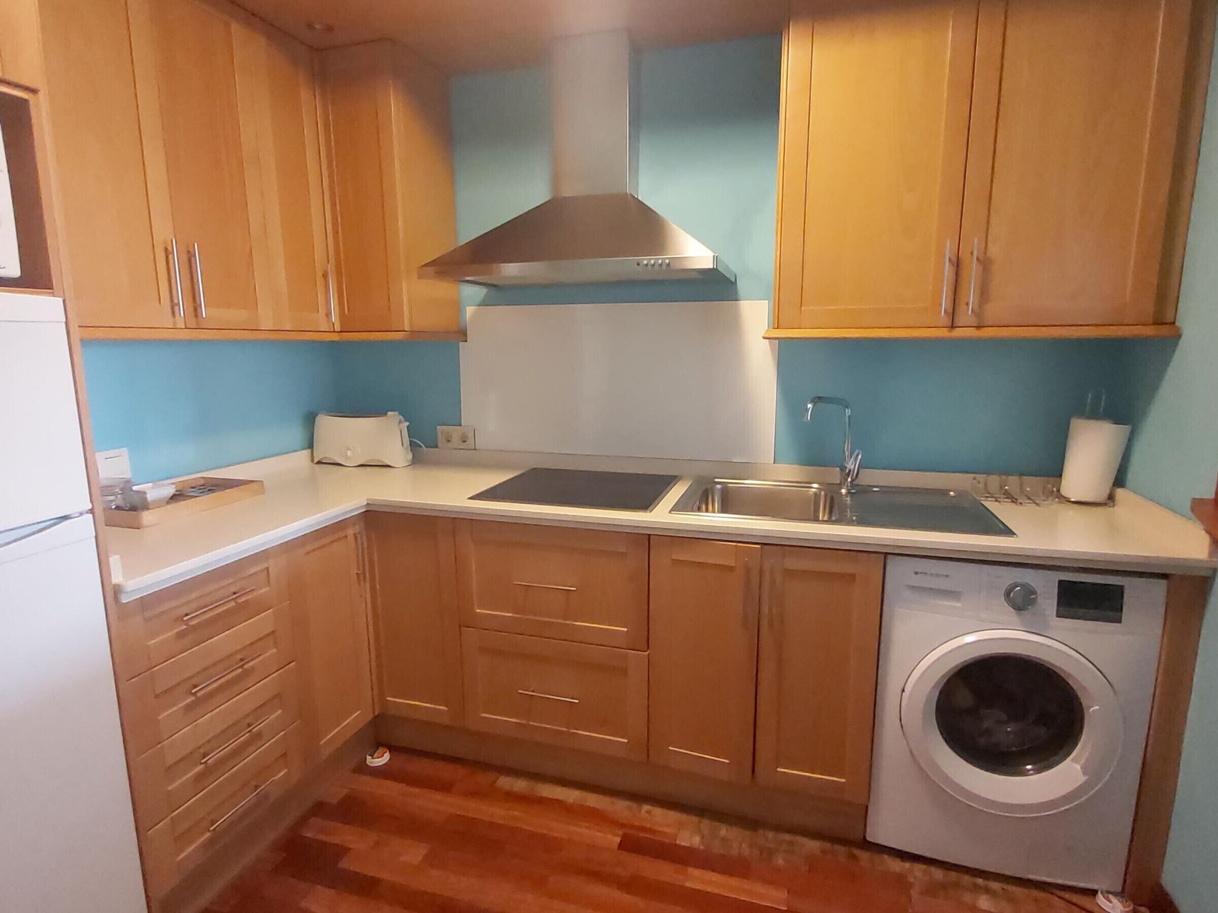Una cocina compacta con armarios de madera, lavadora integrada y pileta de acero inoxidable.