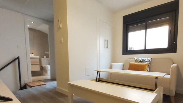 Una sala de estar moderna con un sofá blanco, una mesita y una ventana con persianas.