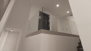 Un interior moderno con balaustrada de vidrio, una escalera e iluminación empotrada en el techo.