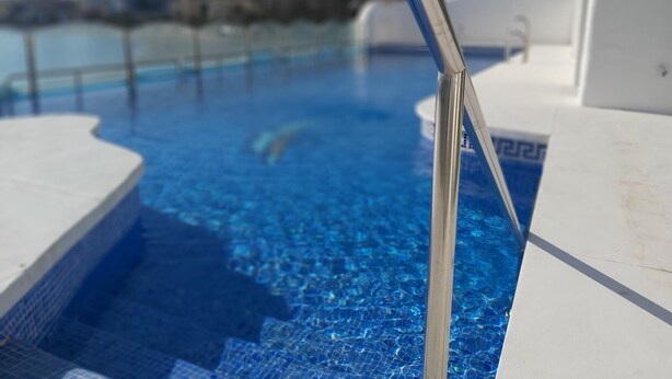 A swimming pool with clear blue water, metal pool ladders, and a lifebuoy on the right side.