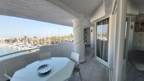 A balcony with a white table and chairs, overlooking a marina with boats and palm trees.