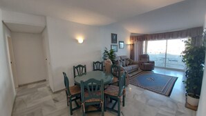 A spacious living room with a dining area, a sofa set, and a large window offering a view.