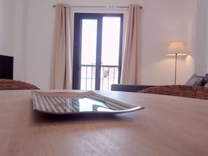 Ein Zimmer mit Holztisch, einer Couch, einer Lampe und einem Fenster mit Vorhängen.