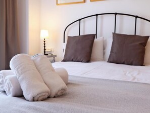 Una cama bien hecha con sábanas blancas y almohadas marrones, una lámpara en una mesita de noche y una cortina a la izquierda.