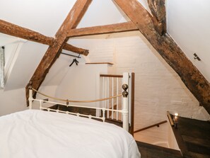 A bedroom with a white bed, wooden beams, a white railing, and a small window.
