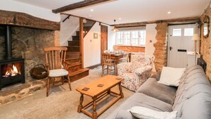 A cozy living room with a stone fireplace, wooden furniture, a sofa, and a dining area with a table and chairs. - Foxden (Sherborne)