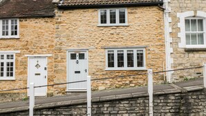 A stone building with a tiled roof, white-framed windows, and a stone wall in front. - Foxden (Sherborne)
