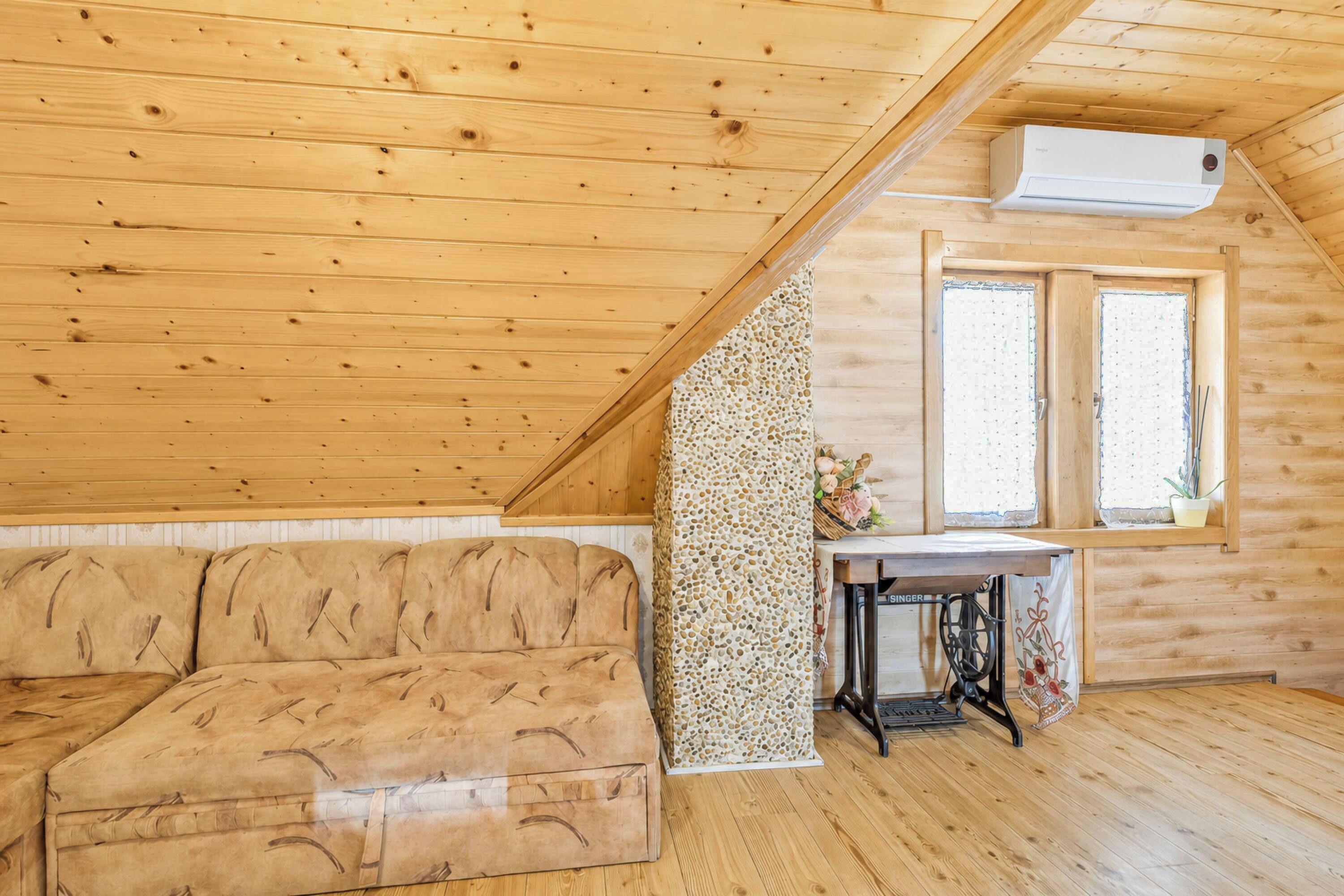 A wooden interior with a sofa, a sewing machine, and a window.