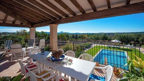 A covered outdoor area with a pool, white furniture, and a view of the countryside.