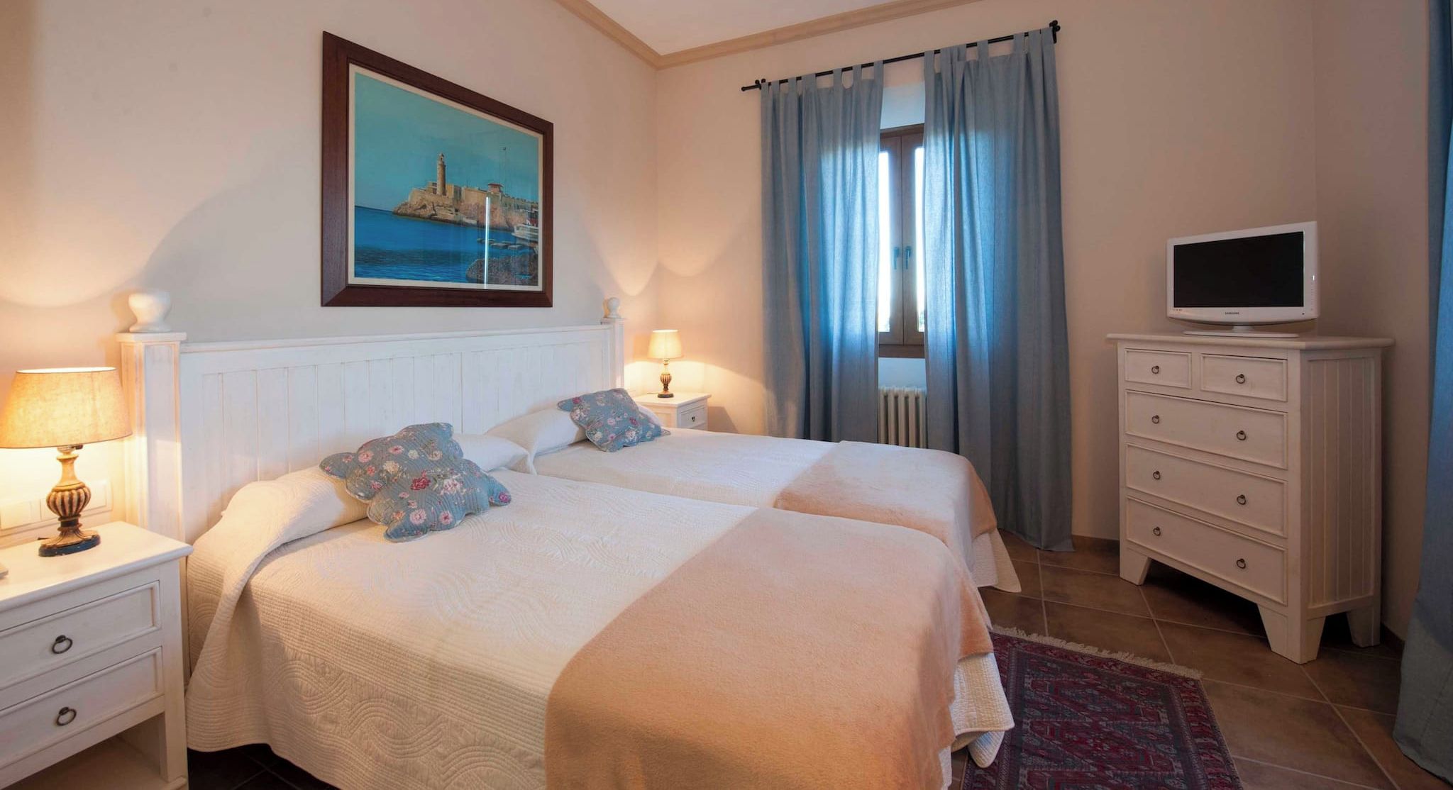 A bedroom with two beds, a television, a painting, and a nightstand with lamps.