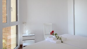 A hotel room with a large window, a bedside table with a lamp, a chair, and a bed with neatly folded towels and a red flower. - Apartment in Malagueta with terrace and sea view (Málaga)