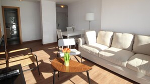 A modern living room with a white sofa, a wooden coffee table with a vase of flowers, and a dining area with a white table and chairs. - Apartment in Malagueta with terrace and sea view (Málaga)
