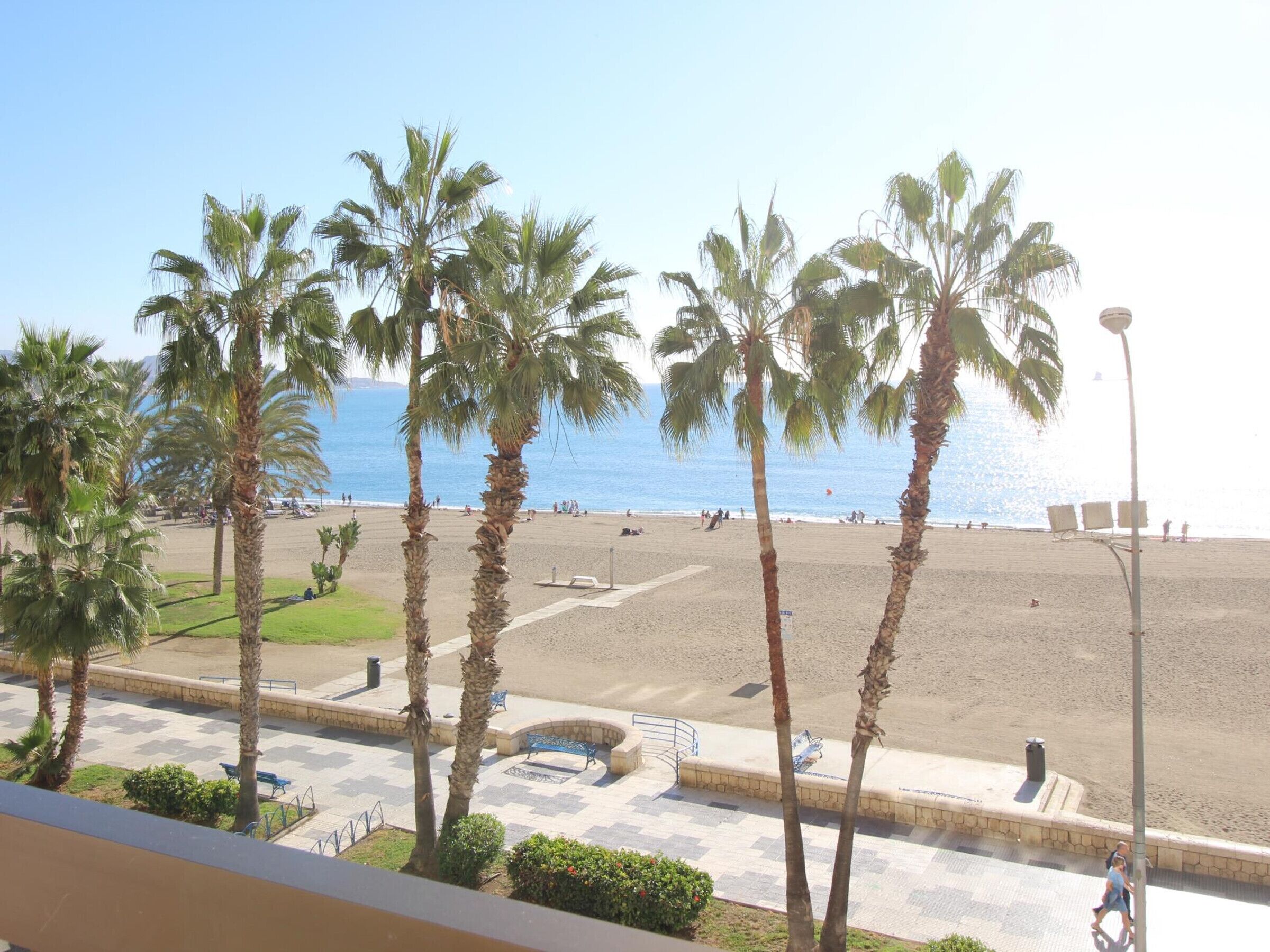 Blick auf einen Strand mit Palmen, einer Promenade und blauem Himmel.