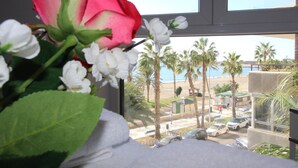A window view of a beachside area with palm trees, parked cars, and a small structure. - Apartment in Malagueta with terrace and sea view (Málaga)