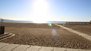 A beach with a clear sky, a sun reflecting off the sand, and a few umbrellas in the distance. - Apartment in Malagueta with terrace and sea view (Málaga)