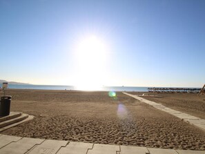 Une plage avec un ciel dégagé, un soleil qui se reflète sur le sable et quelques parasols au loin.