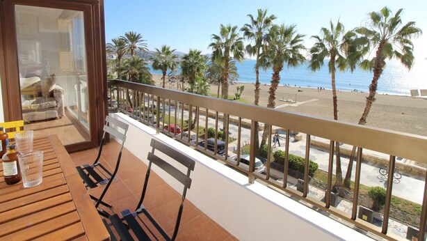 A balcony with a view of the beach, palm trees, and parked cars. - Apartment in Malagueta with terrace and sea view (Málaga)
