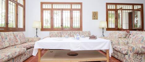A room with a central table, two sofas, and large windows.