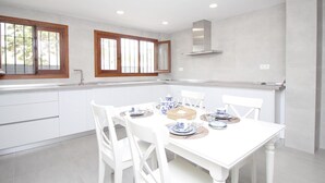 A modern kitchen with white cabinetry, a dining table set for four, and a window with wooden frames. - Luxury Villa with Private Pool, Near Beach and Golf (Málaga)