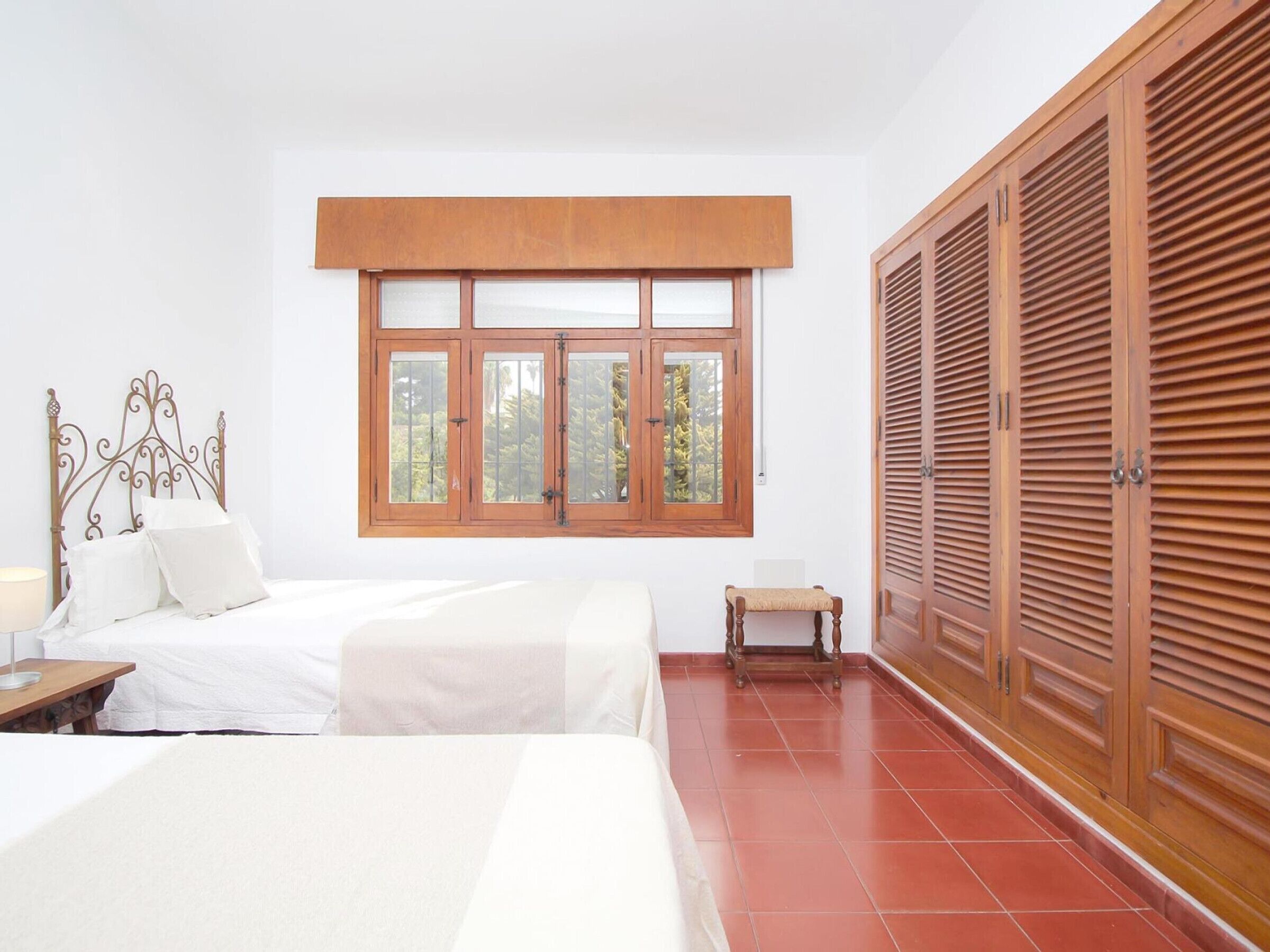 Un dormitorio con cama, ventana, armario y una mesita.