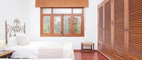 Un dormitorio con cama, ventana, armario y una mesita.