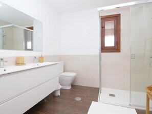 Ein modernes Badezimmer mit Duschkabine aus Glas, einer weißen Toilette und einem großen Spiegel über dem Waschbecken.