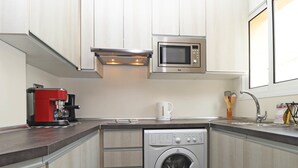 Una cucina compatta con microonde integrato, macchina del caffè e lavatrice a carica frontale.