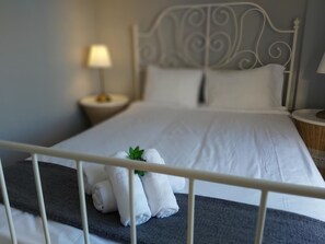 A neatly made bed with white linens and a small green plant on the pillows.