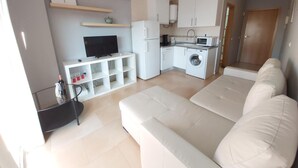 Een moderne woonkamer met een witte bank, een televisie en een klein tv-meubel.