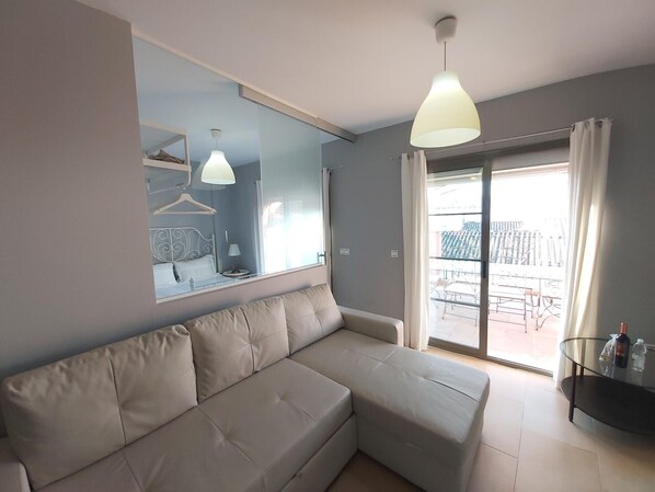 A modern living room with a beige sectional sofa, a large mirror, and a balcony with a glass railing.