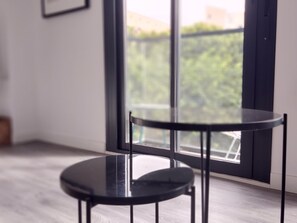 Moderni huone, jossa on pyöreä musta pöytä ja tuoli sekä suuret ikkunat, joista avautuu näkymä vehreään maisemaan.