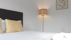 A neatly made bed with white bedding and two pillows, a floor lamp with a beige shade, and a framed abstract artwork on the wall. - Bright 1BR Corner Apt, 3 Balconies, Central Málaga - Ideal for Work & Leisure (Málaga)