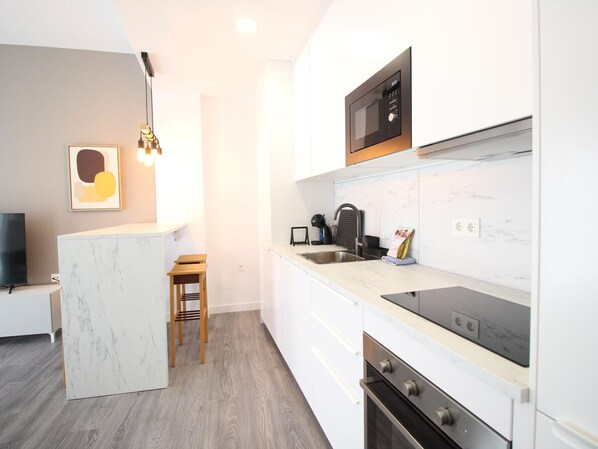 Una cocina moderna con microondas, estufa y pileta integrados. Hay un taburete de madera y un cuadro en la pared.