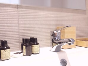 Un baño con un lavamanos moderno, grifo cromado y tres botellas de champú orgánico.
