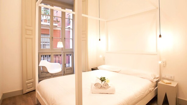 A hotel room with a large bed, a nightstand, a chair, and a window with a view of buildings. - Del Parque Flats Santos Catedral - Cozy Apt in Málaga's Historic Center, Walk to Attractions (Málaga)