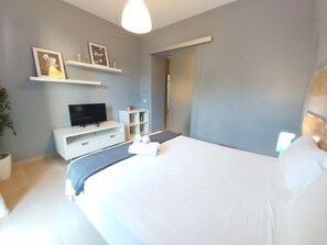 A modern hotel room with a large bed, a flat-screen TV, a small desk, and a mirror. - Charming Apartment in Historic Málaga Center, Near Museums and Beach (Málaga)