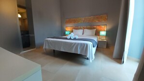 A modern hotel room with a large bed, two bedside tables with lamps, a painting on the wall, and a view of the hallway.