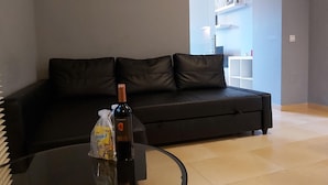 A modern living room with a black leather sofa, a glass coffee table, and a bottle of wine.