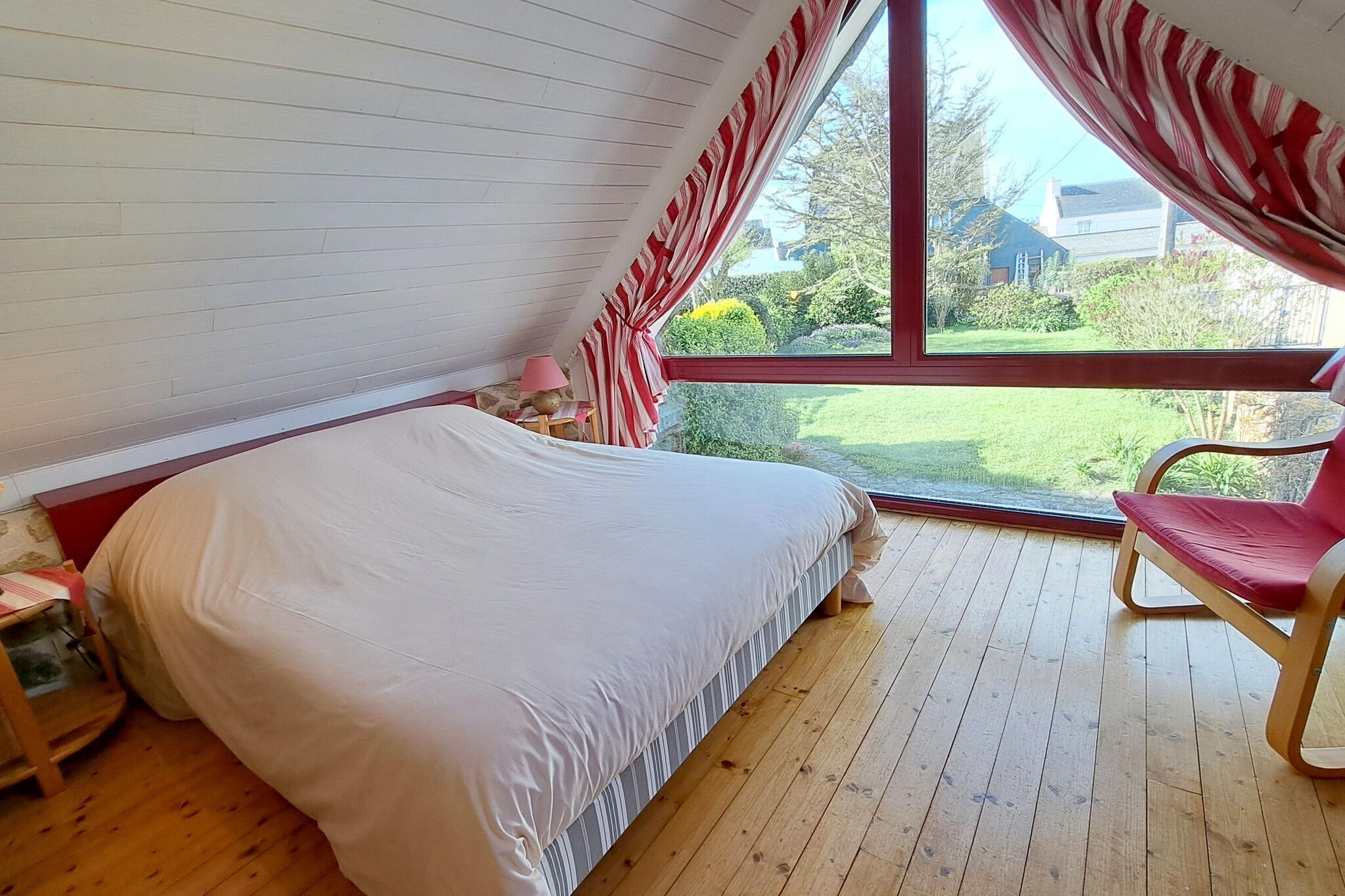 Une chambre avec une grande fenêtre, un lit, une chaise et une petite table.