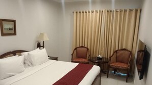 A hotel room with a large bed, two chairs, a small table, a lamp, and a television. - Welcome Hotel Islamabad (Islamabad)