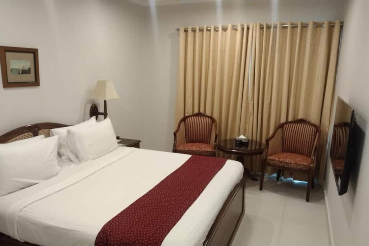 A hotel room with a large bed, two chairs, a small table, a lamp, and a television.
