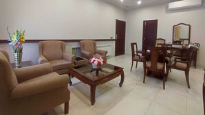 A spacious living room with beige sofas, a glass coffee table, and a dining area with wooden furniture. - Welcome Hotel Islamabad (Islamabad)