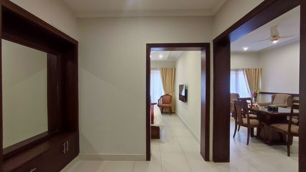 A hotel room with a large bed, a TV, and a dining area with chairs and a table. - Welcome Hotel Islamabad (Islamabad)